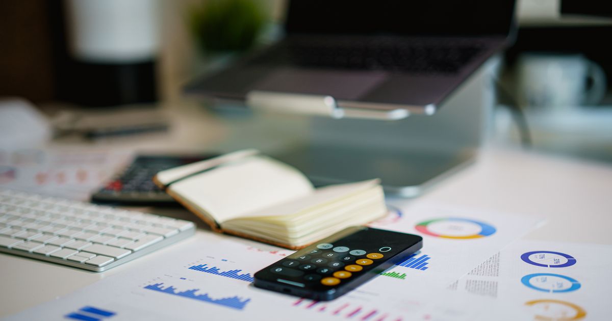 Mesa de trabalho com laptop, calculadora e gráficos financeiros sob luz natural